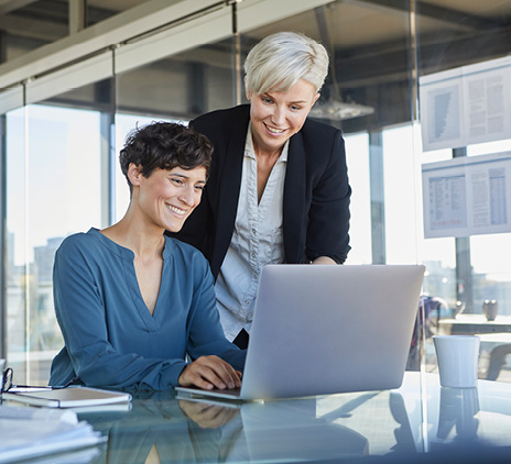 two smiling businesswomen sharing laptop