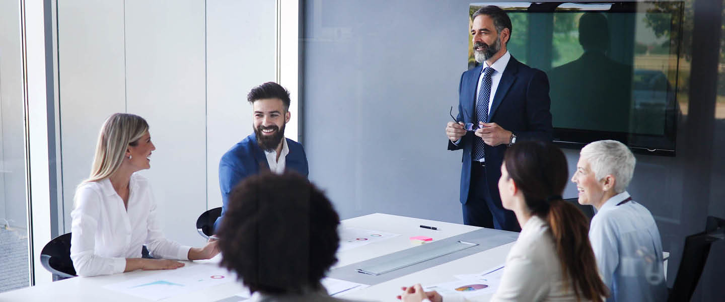 Zakelijke vergadering met mensen in formele kleding. Allemaal heel vrolijk dus het gaat goed met hun bedrijf. Een persoon staat aan het hoofd van de tafel dat is waarschijnlijk de directeur.