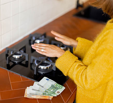 Vrouw die boven haar fornuis, haar handen warmt. De kosten hiervan liggen naast haar op haar aanrecht.